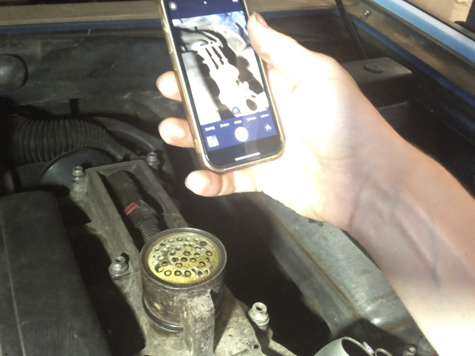 A mechanic photographs an oil-fouled engine component with a phone so the customer can see it.